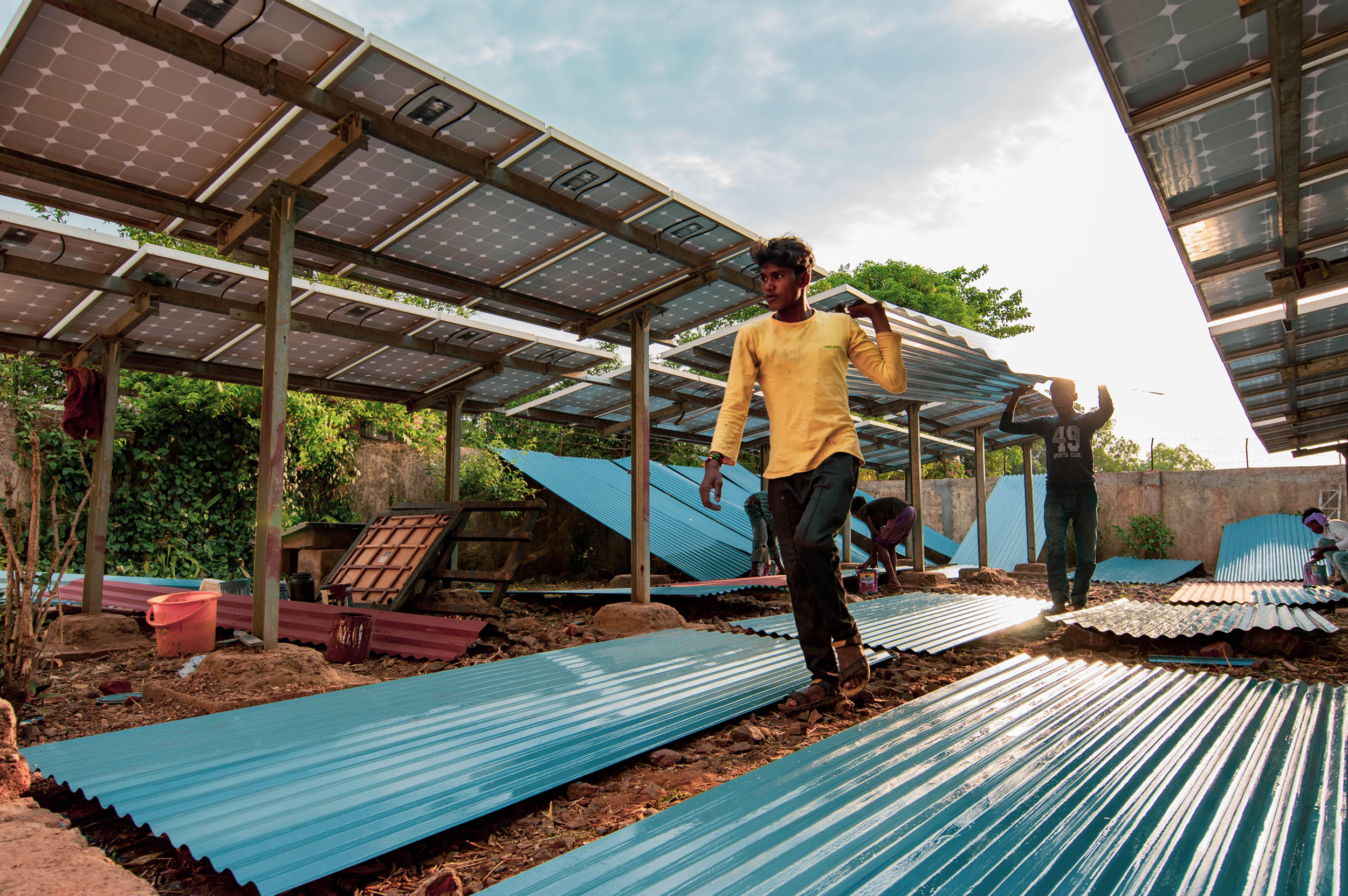 Mohan Majhi (L), age 18, and Hiran Naik (R), age 23, carry a finished roofing sheet to be placed on the roof. Photo credit: Ajaya Behera.