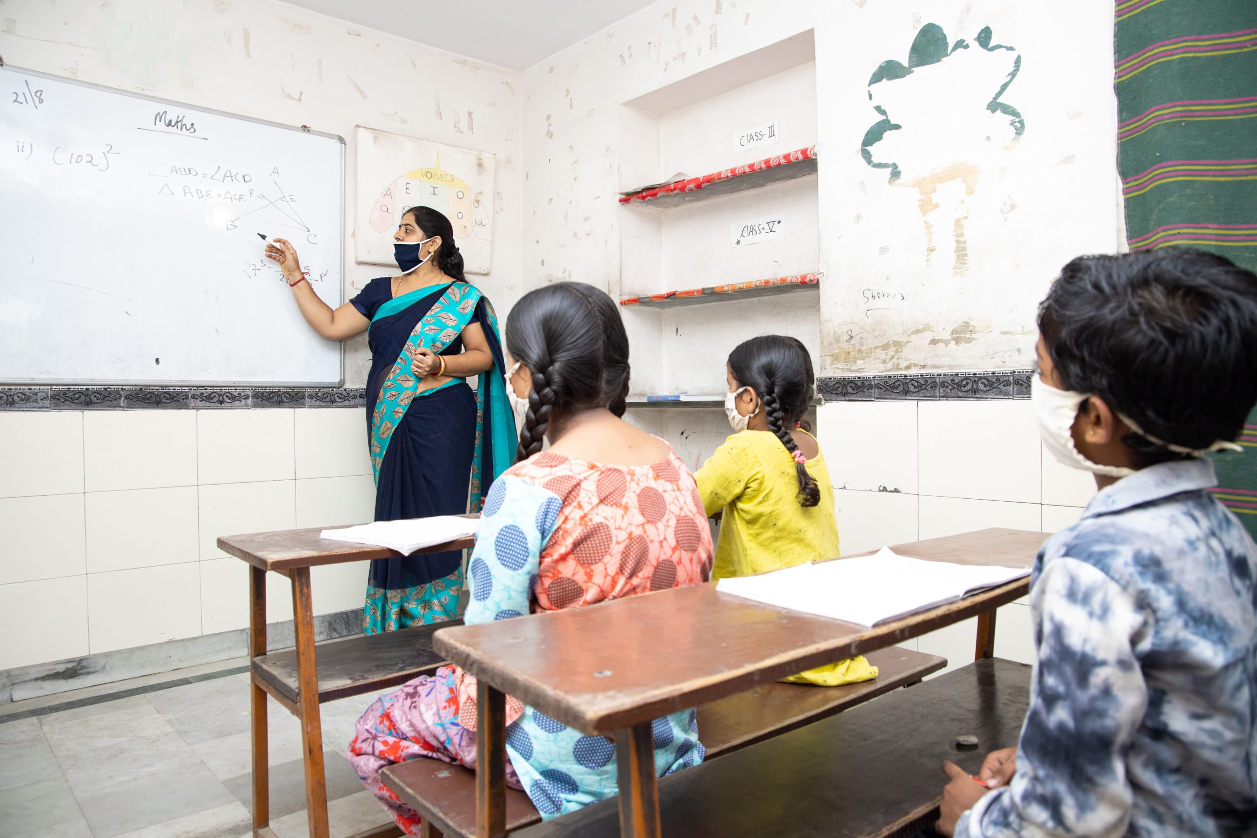 Indian teacher and students wearing face masks maintaining social distancing study in classroom back at school during covid19 pandemic.