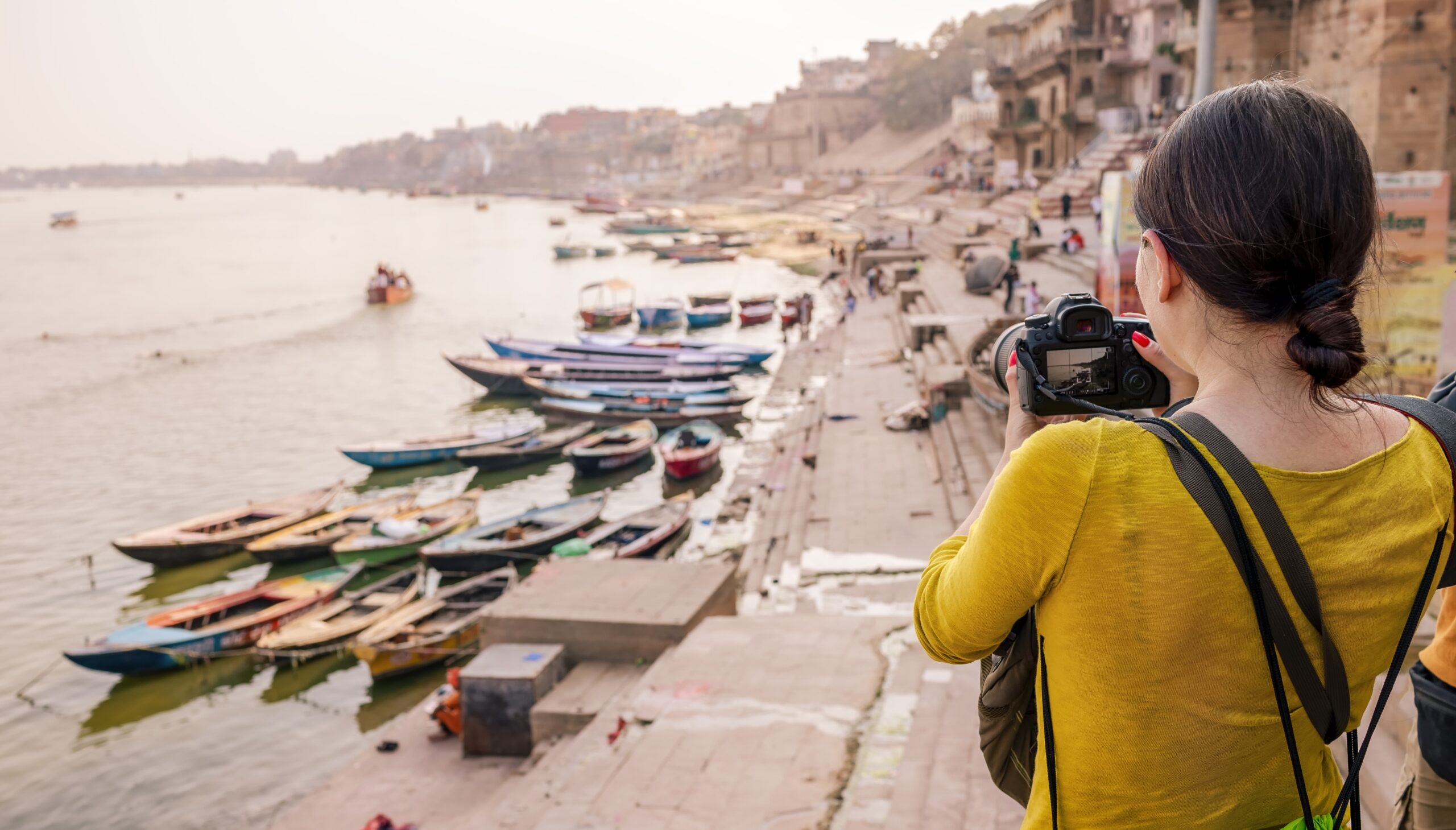 A tourist woman takes pictures of boats on the Ganges River in Varanasi.